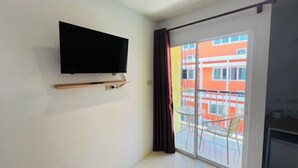 A room with a flat-screen TV mounted on the wall, a sliding glass door leading to an outdoor balcony with chairs, and a kitchen area with a refrigerator. - Pattaya Inn hotel (Pattaya)