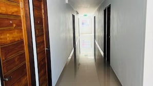 A long, narrow hallway with wooden doors on one side and plain walls on the other. - Pattaya Inn hotel (Pattaya)