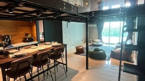 A modern dining area with a long table, chairs, and a kitchen in the background.