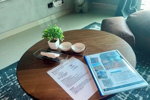 Une table ronde en bois, sur laquelle se trouvent une petite plante en pot, deux bols blancs, une boîte de mouchoirs et une brochure.