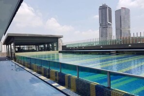 A swimming pool with a tiled edge, a covered seating area, and a view of tall buildings in the background. - Lily & Loft - The Grand Sofo, Petaling Jaya (Petaling Jaya)