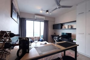 Une chambre d’hôtel moderne équipée d’un lit, d’un bureau avec un ordinateur portable, d’une télévision et d’une grande fenêtre.