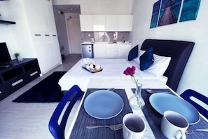 Ein modernes Hotelzimmer mit Bett, Essbereich, Küchenzeile und Fernseher.