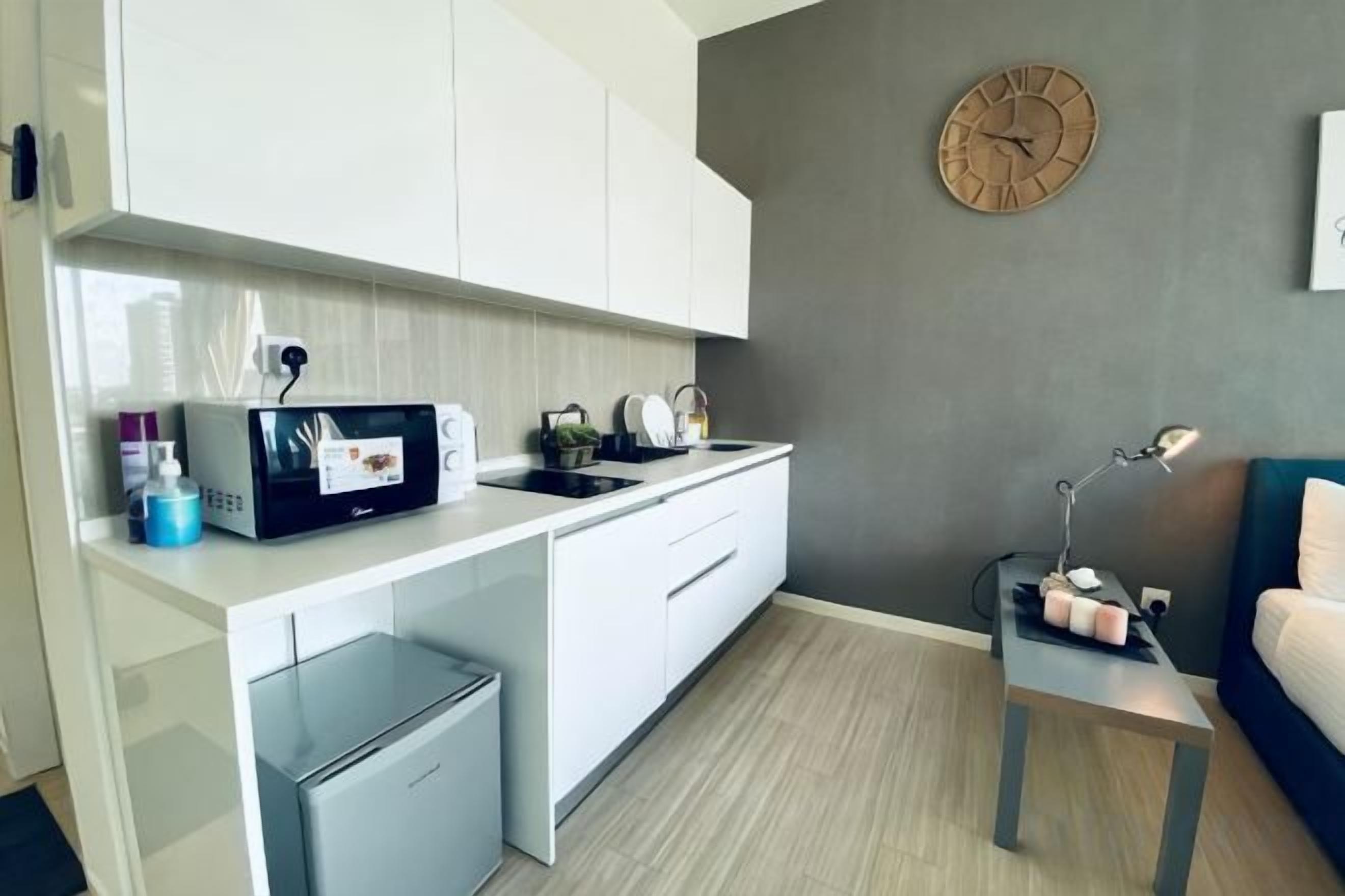 A compact kitchen with white cabinets, a microwave, a small refrigerator, and a sink.
