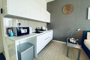 Eine kompakte Küche mit weißen Schränken, einer Mikrowelle, einem kleinen Kühlschrank und einem Spülbecken.
