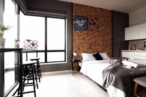 Un dormitorio moderno con un ventanal grande, una cama, un escritorio y una kitchenette.