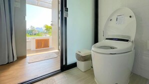 A modern bathroom with a toilet, a small trash bin, and a glass door leading to an outdoor area. - 101 Space Station (Lan Sak)