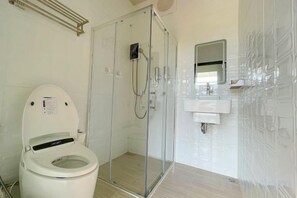 A bathroom with a toilet, a glass-enclosed shower, and a sink with a mirror.