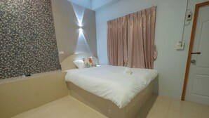 A bedroom with a bed, a headboard, a wall with a textured pattern, a curtain, and a door. - Sleepdive Samaesan (Sattahip)