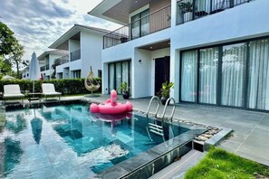 A modern pool area with a floating pink toy, lounge chairs, and a two-story building with large windows.