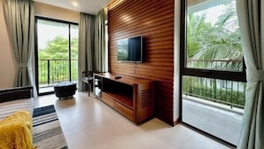 Una sala de estar moderna con un televisor grande, paneles de madera, un sofá y un balcón con vistas a zonas verdes.