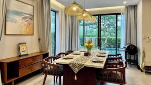Comedor con una mesa grande dispuesta para cuatro personas, rodeada de sillas de madera, con una lámpara colgante arriba.