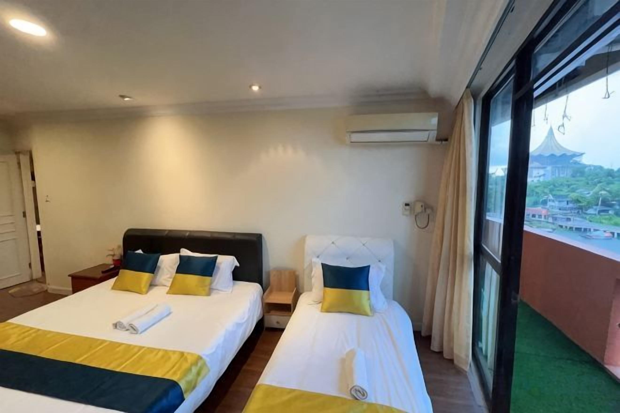 A hotel room with two beds, a view of a building through a window, and an air conditioning unit on the wall.