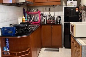 Une cuisine avec des meubles de rangement en bois, une cuisinière, un four à micro-ondes et divers ustensiles de cuisine.