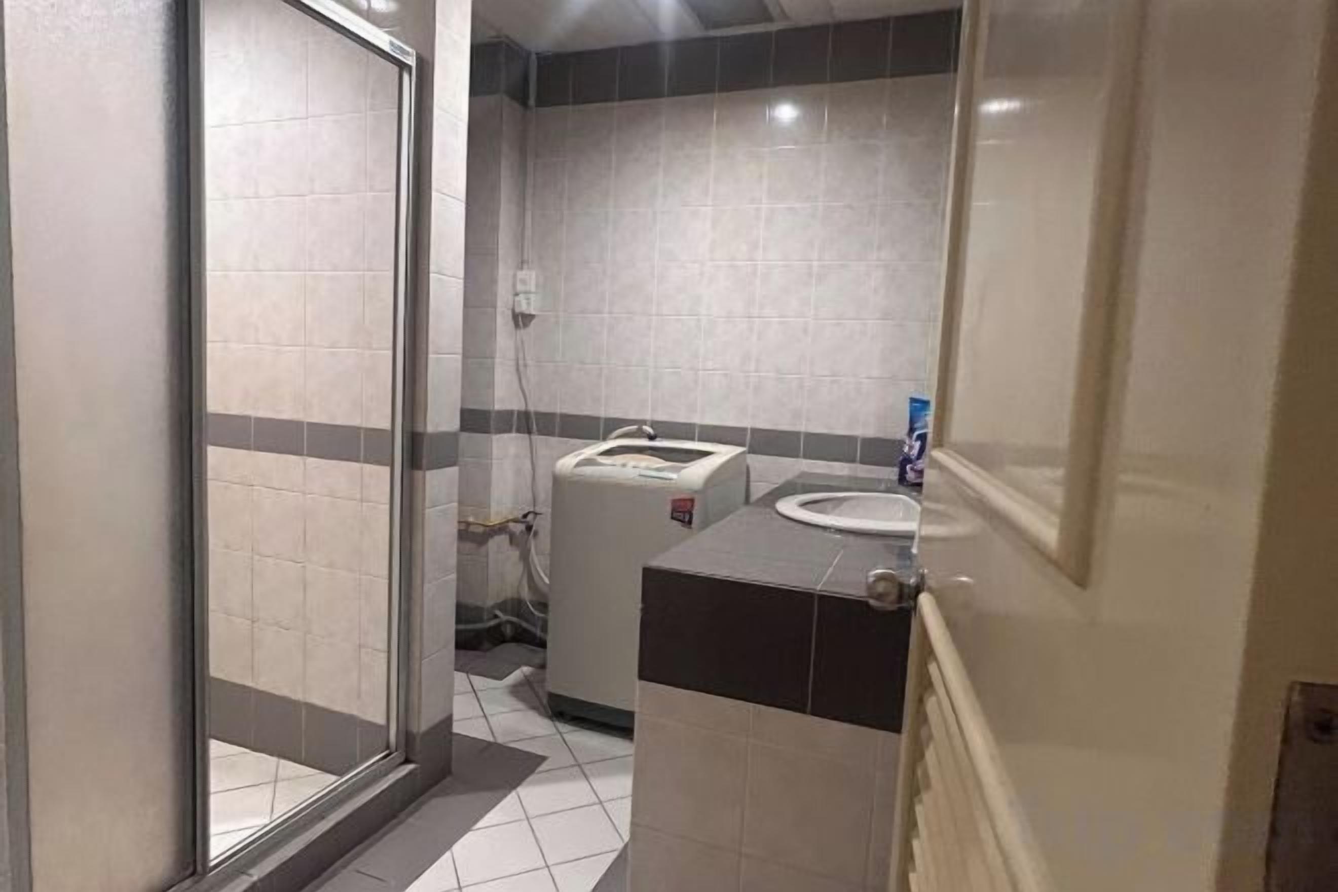 A bathroom with a glass door, a sink, a mirror, and a towel dispenser.
