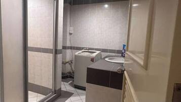 A bathroom with a glass door, a sink, a mirror, and a towel dispenser.