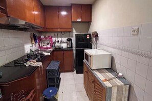 Une cuisine de taille réduite, dotée de meubles en bois, d’un réfrigérateur noir, d’un four à micro-ondes et d’un évier.