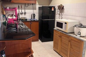 Une cuisine avec un réfrigérateur noir, un four à micro-ondes et un cuiseur à riz posés sur le plan de travail.
