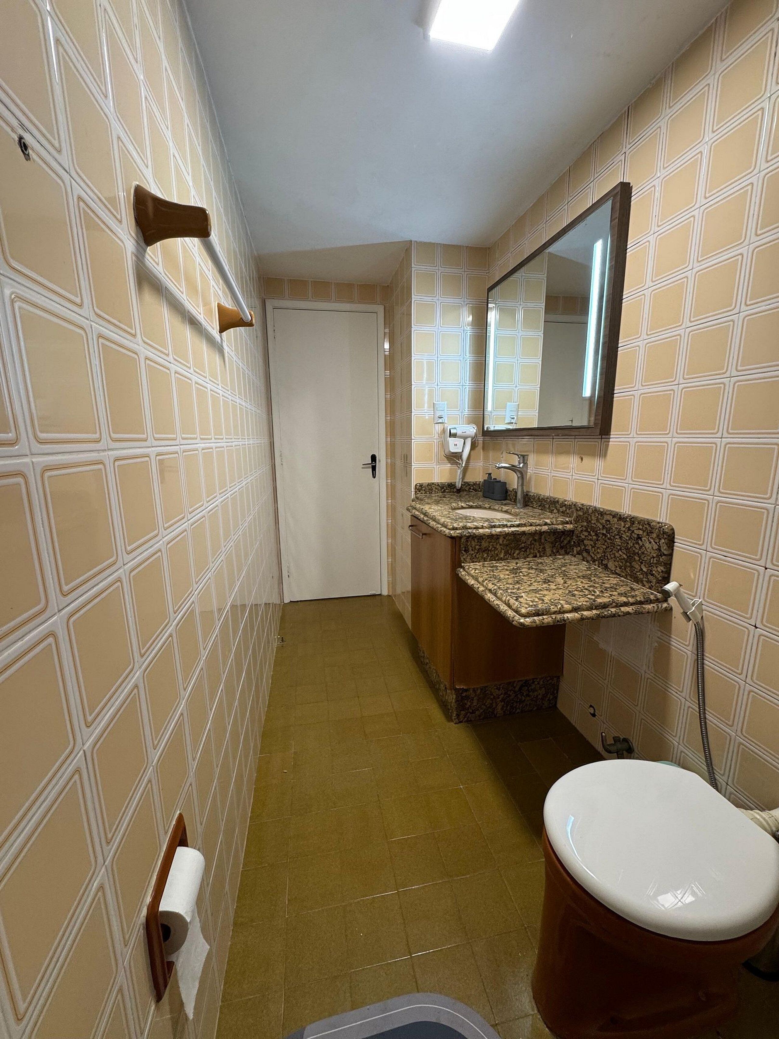 Ein schmales Badezimmer mit Toilette, Waschbecken und Spiegel.