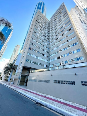 A multi-story building with a modern architectural design, featuring a prominent corner entrance and a visible balcony on the ground floor. - Edificil Antares (Balneário Camboriú)