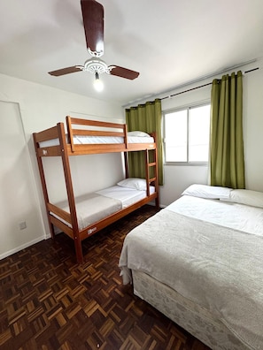A bunk bed room with a ceiling fan, a window with curtains, and a patterned wooden floor. - Edificil Antares (Balneário Camboriú)
