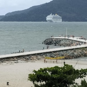 Un muelle se adentra en aguas tranquilas con un crucero a lo lejos, rodeado de terreno rocoso y vegetación.