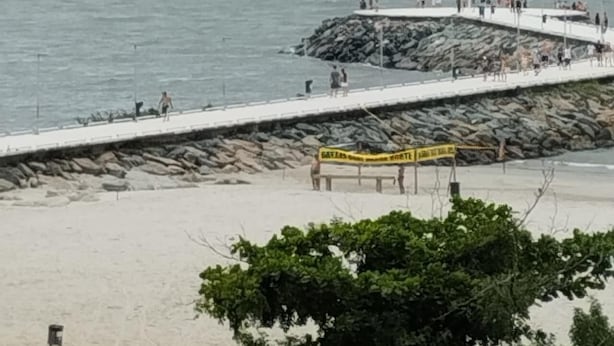 A pier extending into calm water with a cruise ship in the distance, surrounded by rocky terrain and greenery. - Edificil Antares (Balneário Camboriú)