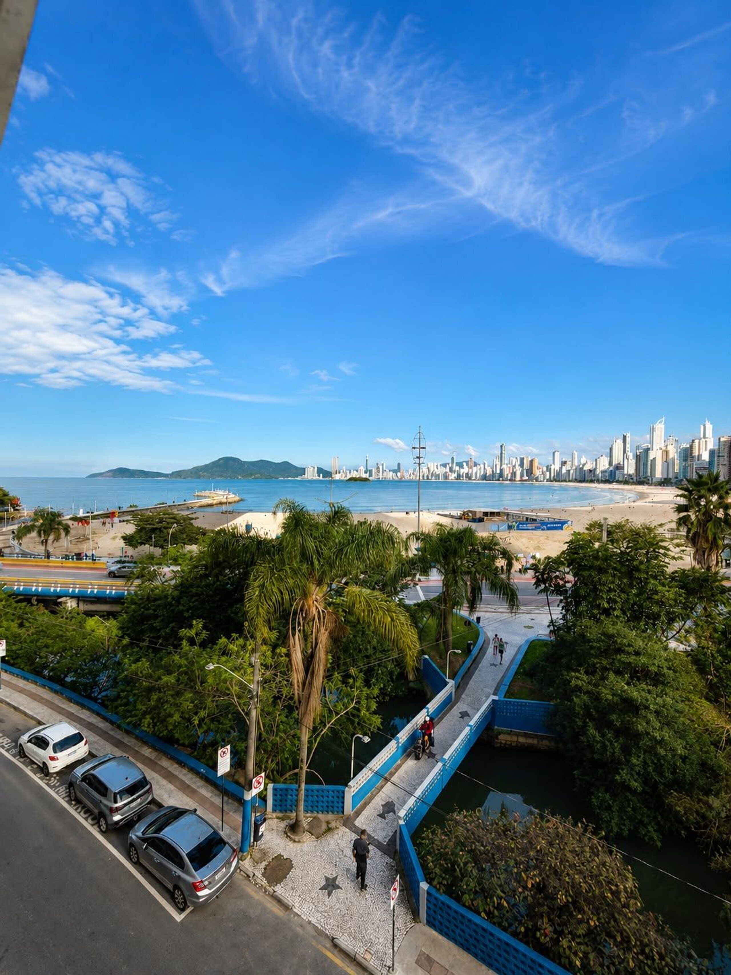 A coastal cityscape with a clear sky, a beach, and a bridge connecting two areas.