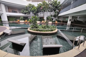 An indoor swimming pool with lounge chairs and a central plant arrangement. - Mulberry Verve Suites KL Mid Valley 4Pax 2 Bedroom (Kuala Lumpur)