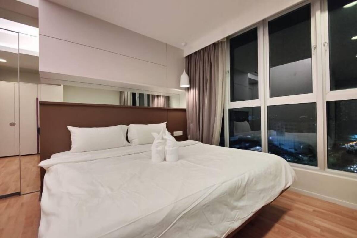A hotel room with a large bed, a wooden headboard, a nightstand, and a window with curtains.