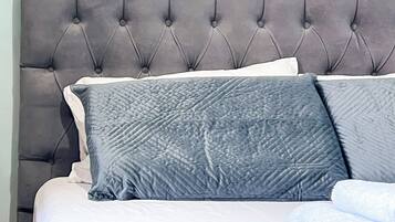A bed with a tufted headboard, grey bedding, and a folded white towel.