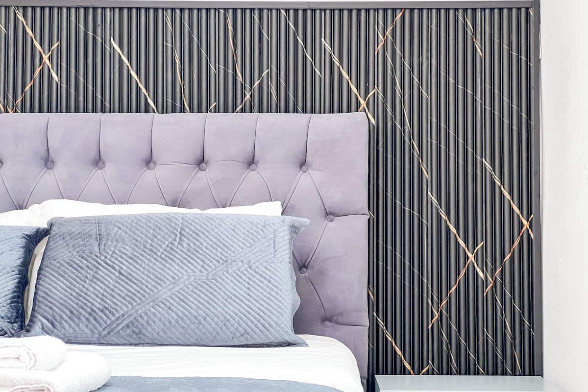 A bed with a tufted headboard, a white pillow, a grey pillow, and a folded white towel.