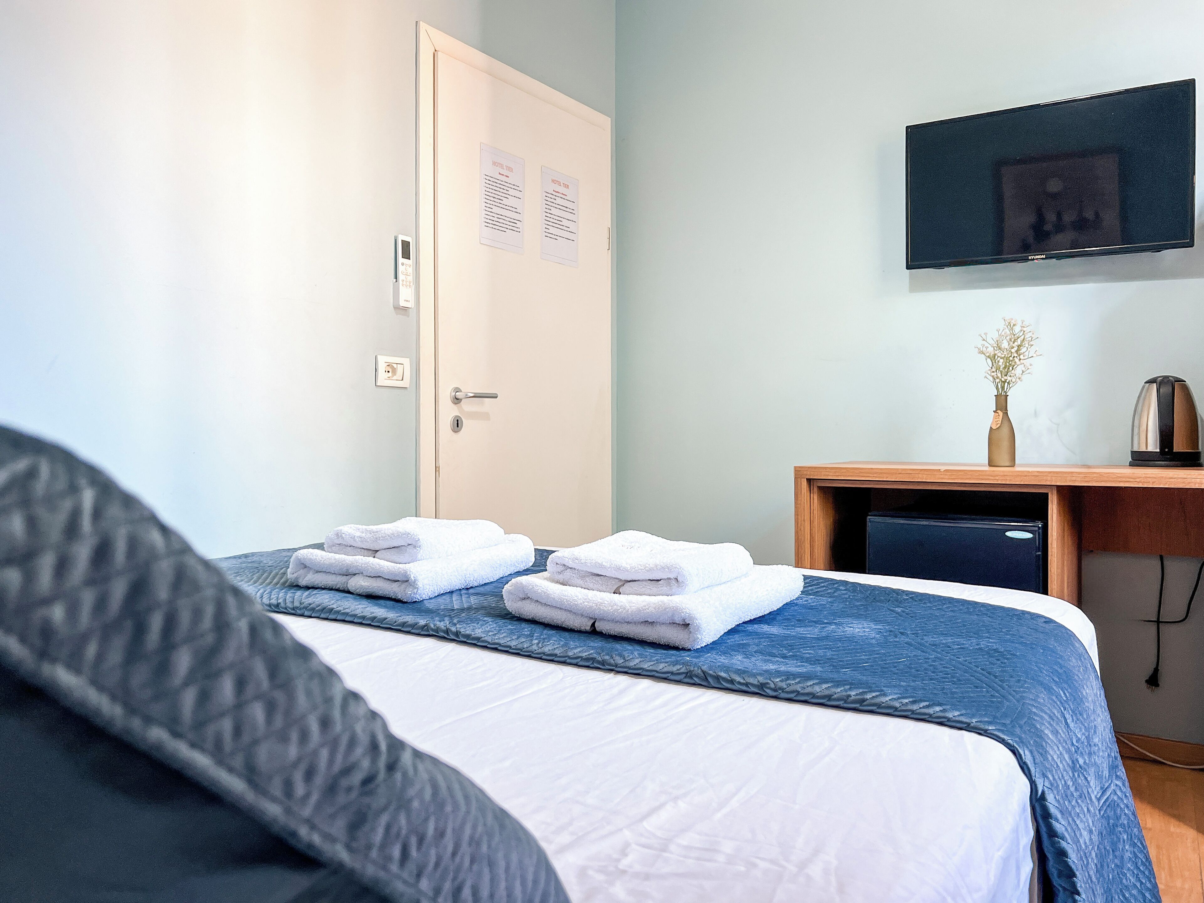 A hotel room with a bed, a desk, a television, and a door with a lock and a light switch.