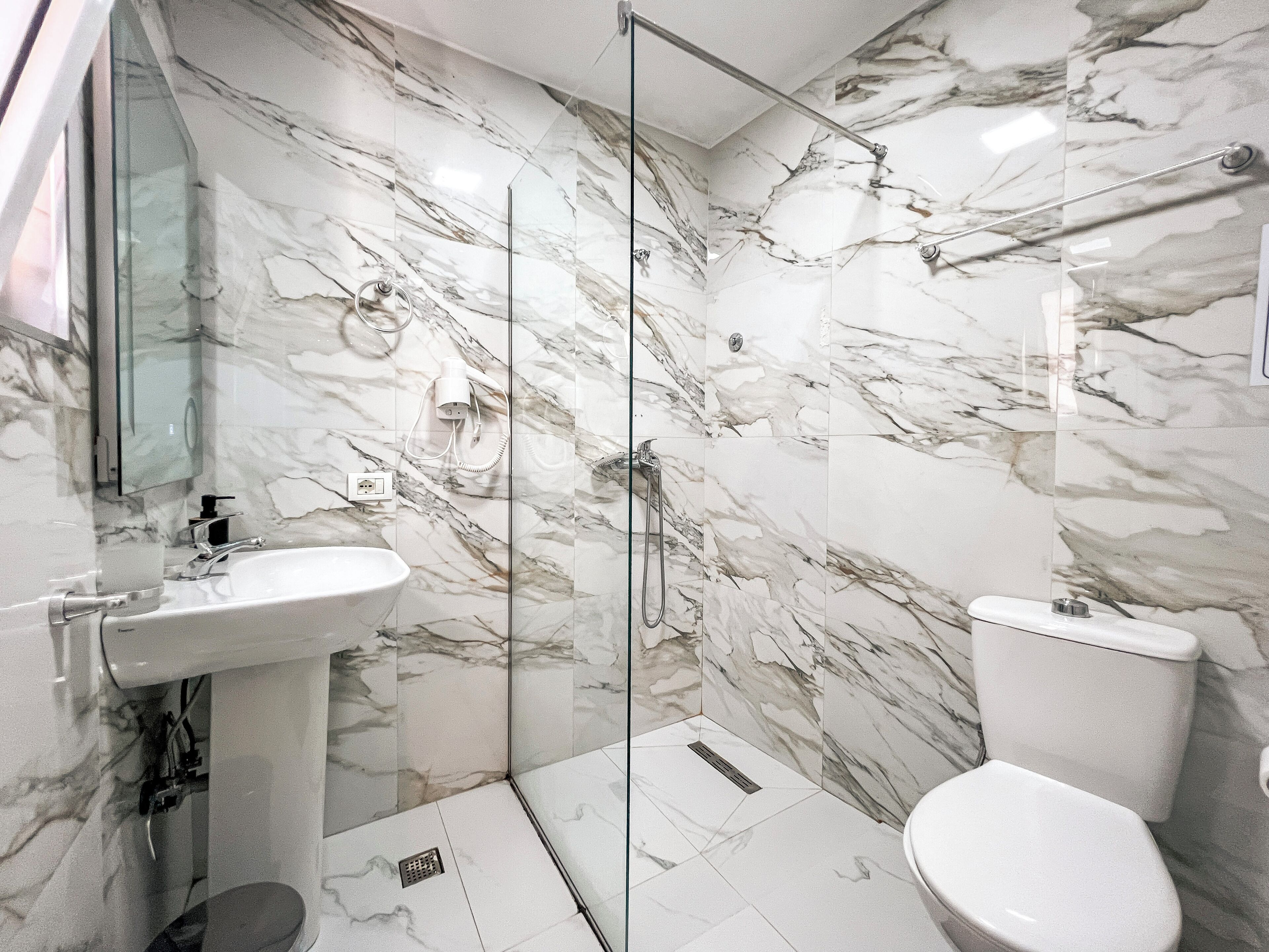 Une salle de bain avec un mur en marbre, une cabine de douche en verre, un lavabo blanc et des toilettes.
