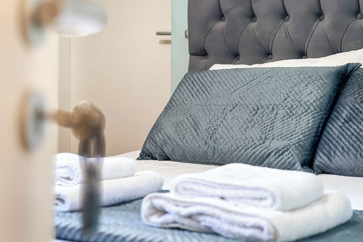 A neatly made bed with a grey headboard, a folded white towel, and a blue pillow.
