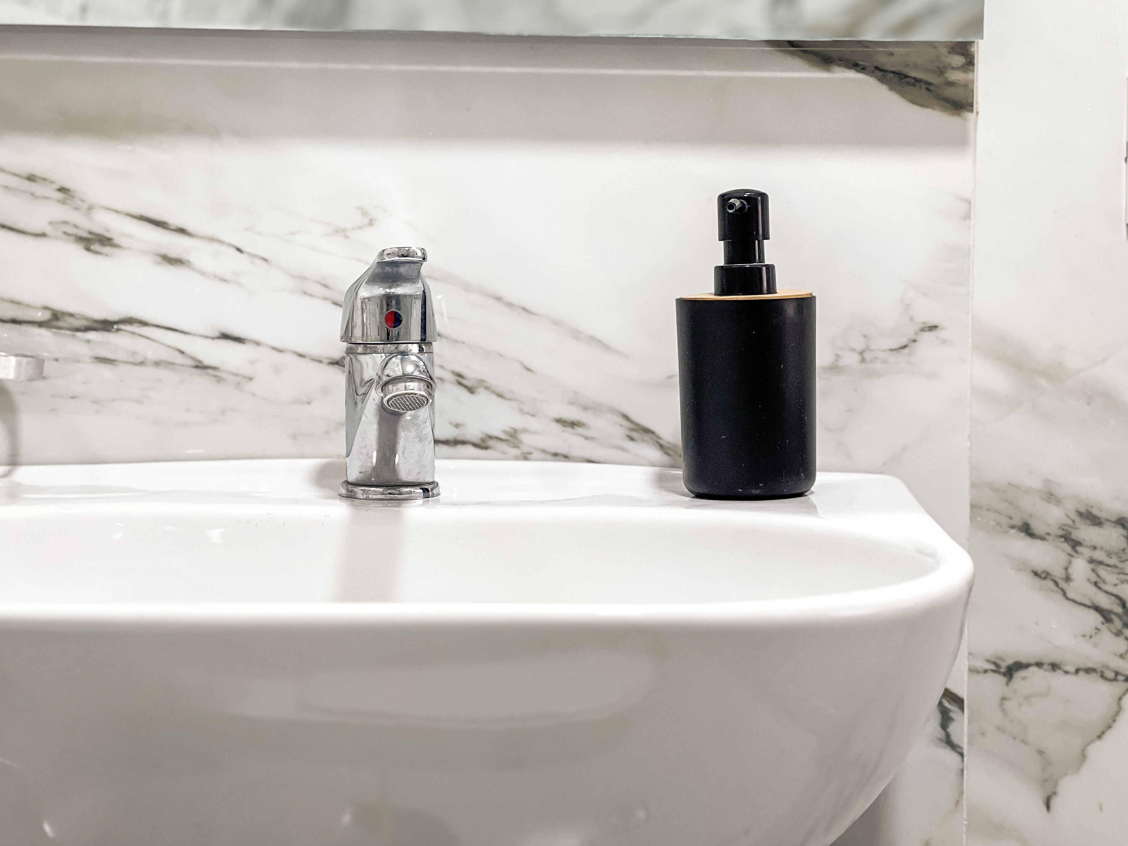 Ein Badezimmerwaschbecken mit modernem Wasserhahn und einer schwarzen Flasche auf der Ablagefläche.