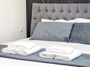 A neatly made bed with grey and white bedding, a grey headboard, and two folded white towels on a grey pillow. - Hotel Tier Center (Tirana)