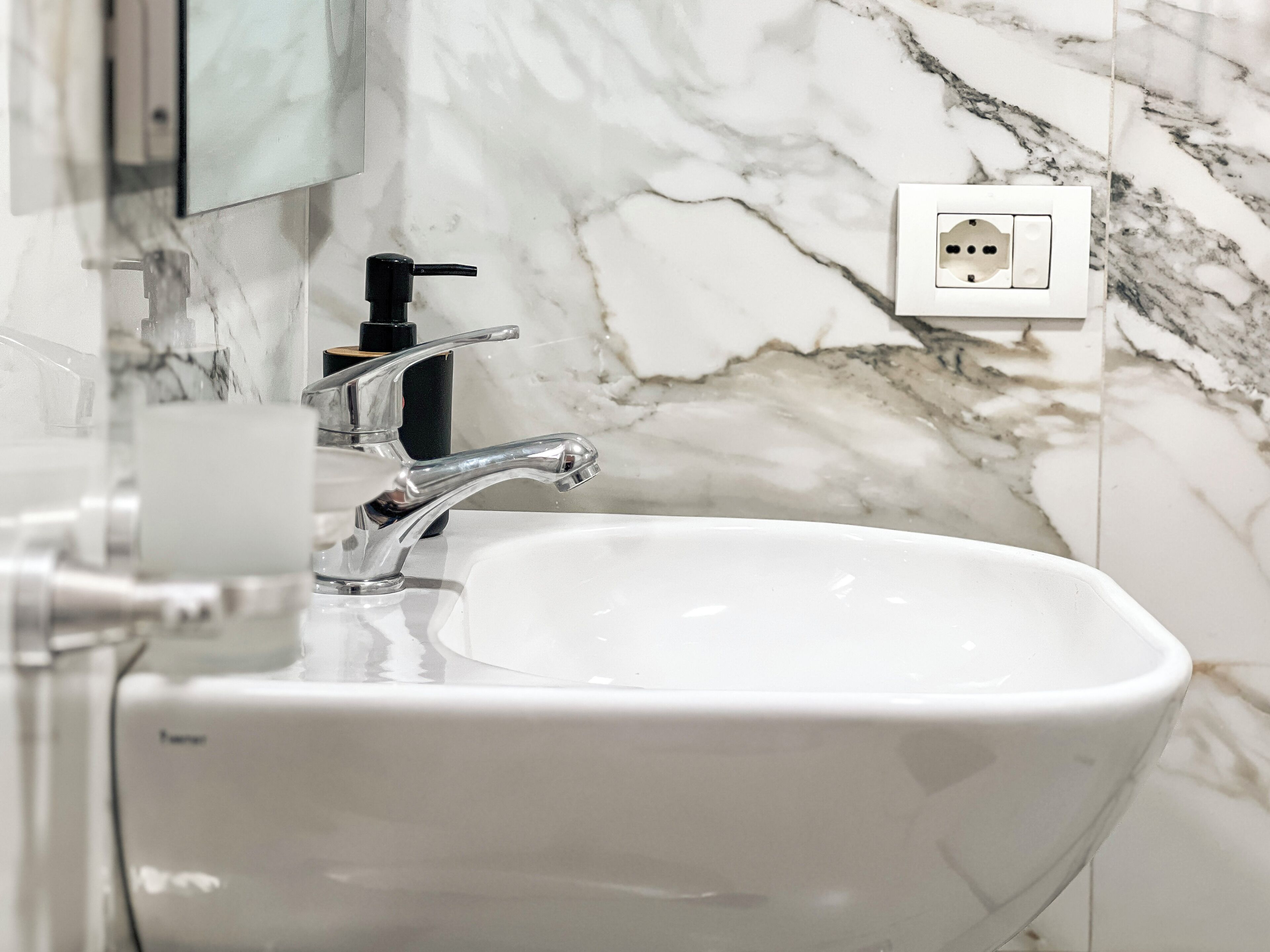 Une salle de bain avec un lavabo blanc, un distributeur de savon noir et un pare-éclaboussures en marbre.