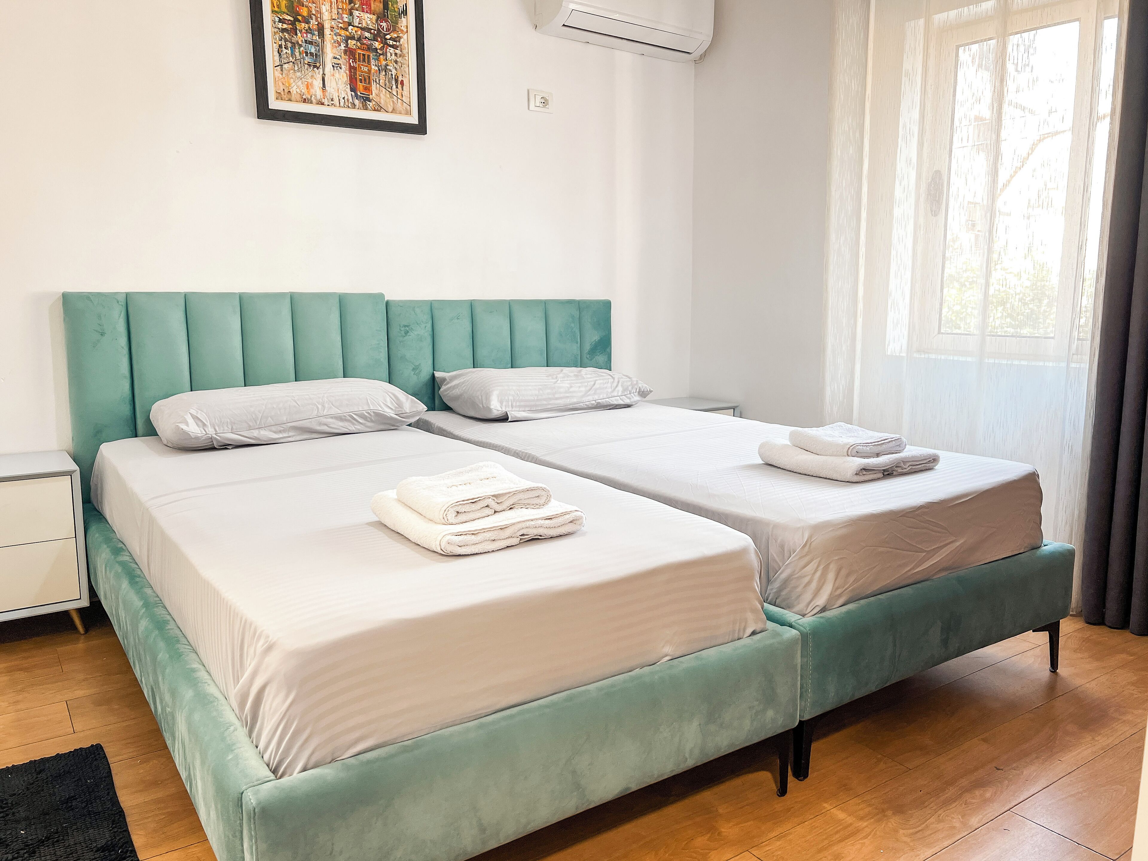 A double bed with a teal headboard, two white pillows, and a folded white towel on the bed.