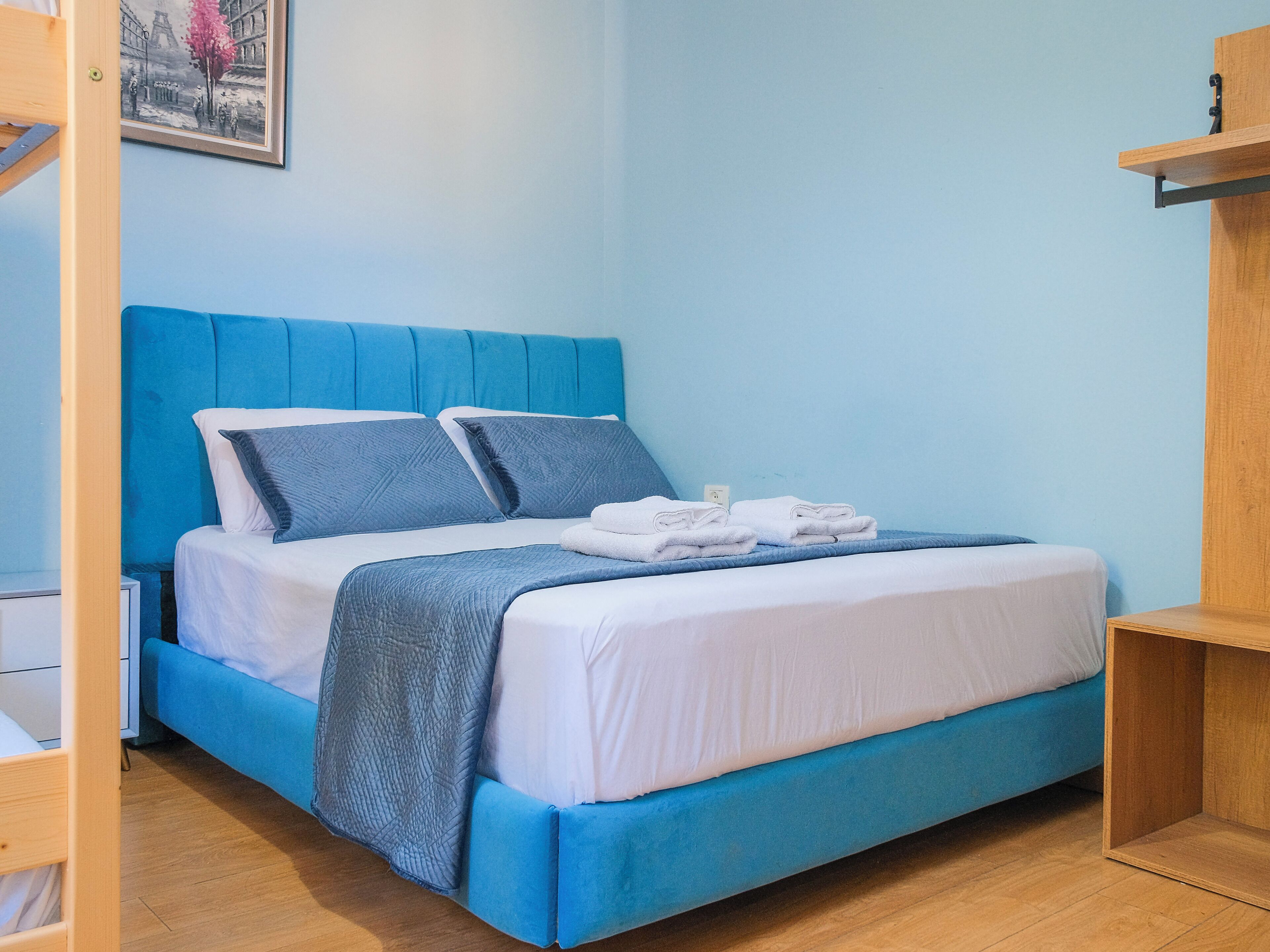 Un lit bien fait, avec une literie bleue et des oreillers, une couverture blanche et des serviettes pliées, le tout posé sur un plancher en bois.