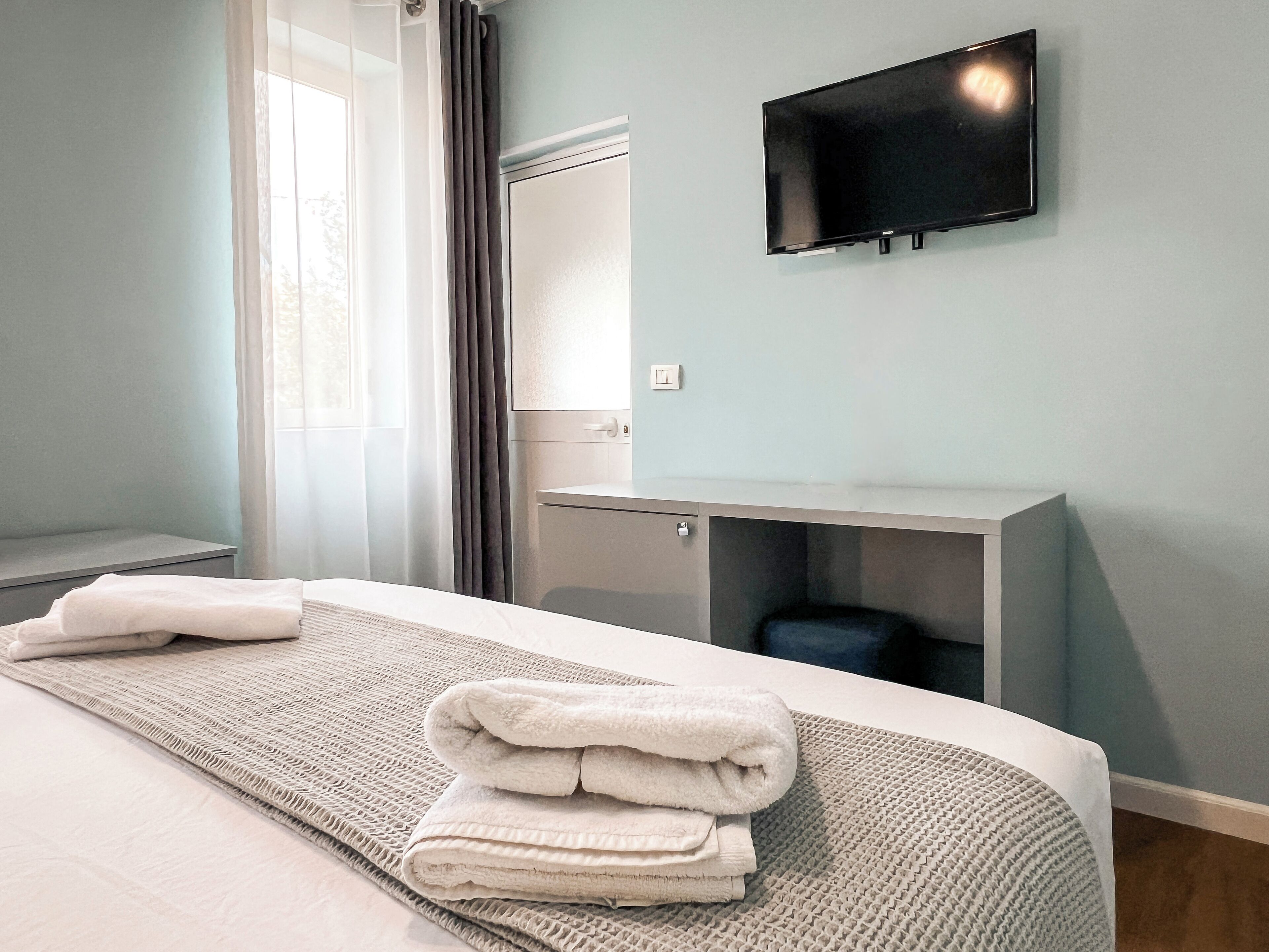 A hotel room with a bed, a TV mounted on the wall, a mirror, and a small desk.