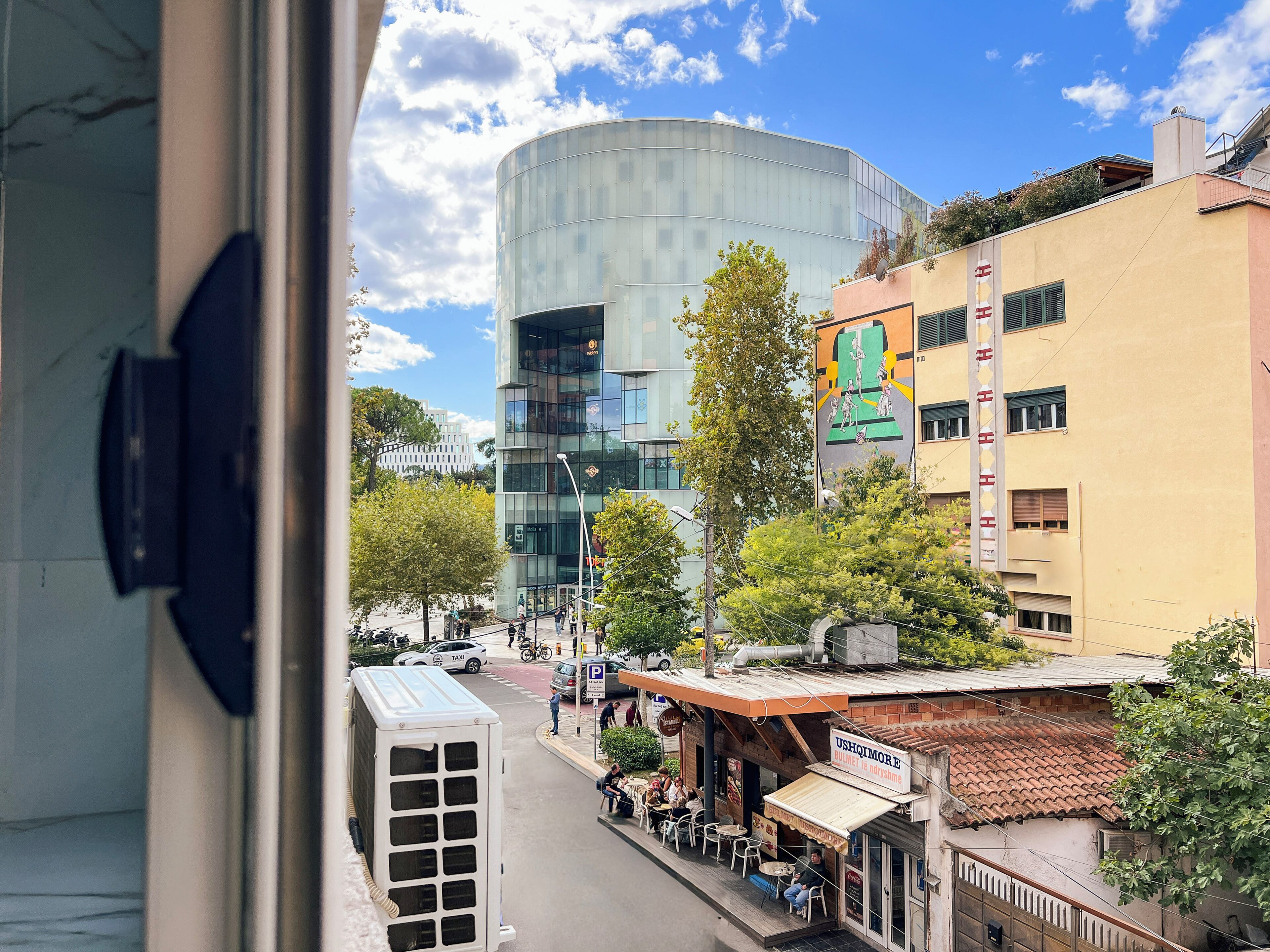 A view of a street with a modern building, a restaurant, and parked cars.