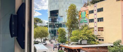 A view of a street with a modern building, a restaurant, and parked cars.