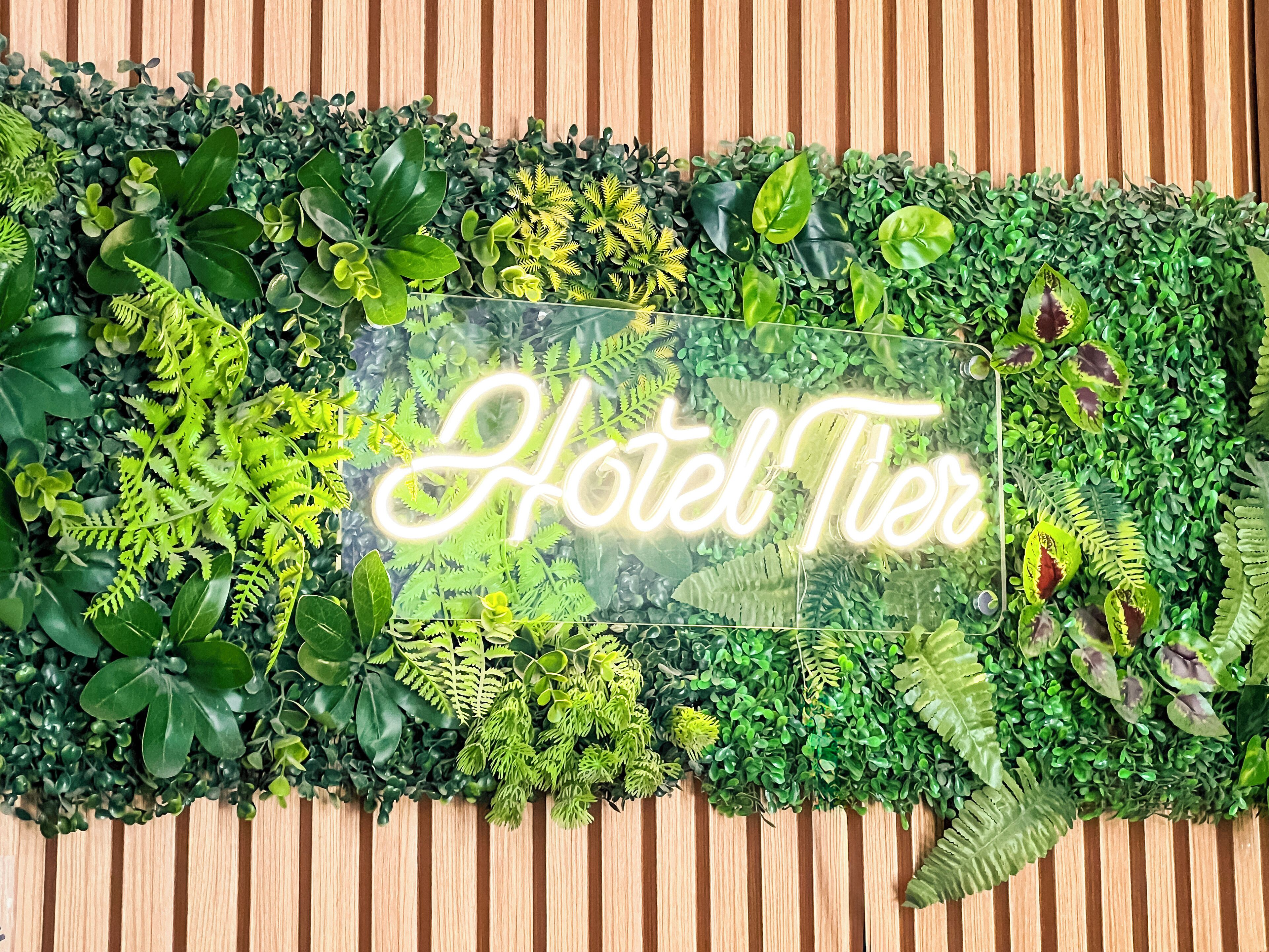Μια φωτεινή επιγραφή νέον με την ένδειξη «Hotel Tier» μέσα σε ένα καταπράσινο περιβάλλον.