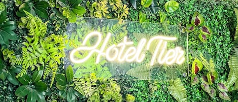 A neon sign reading "Hotel Tier" amidst lush greenery.