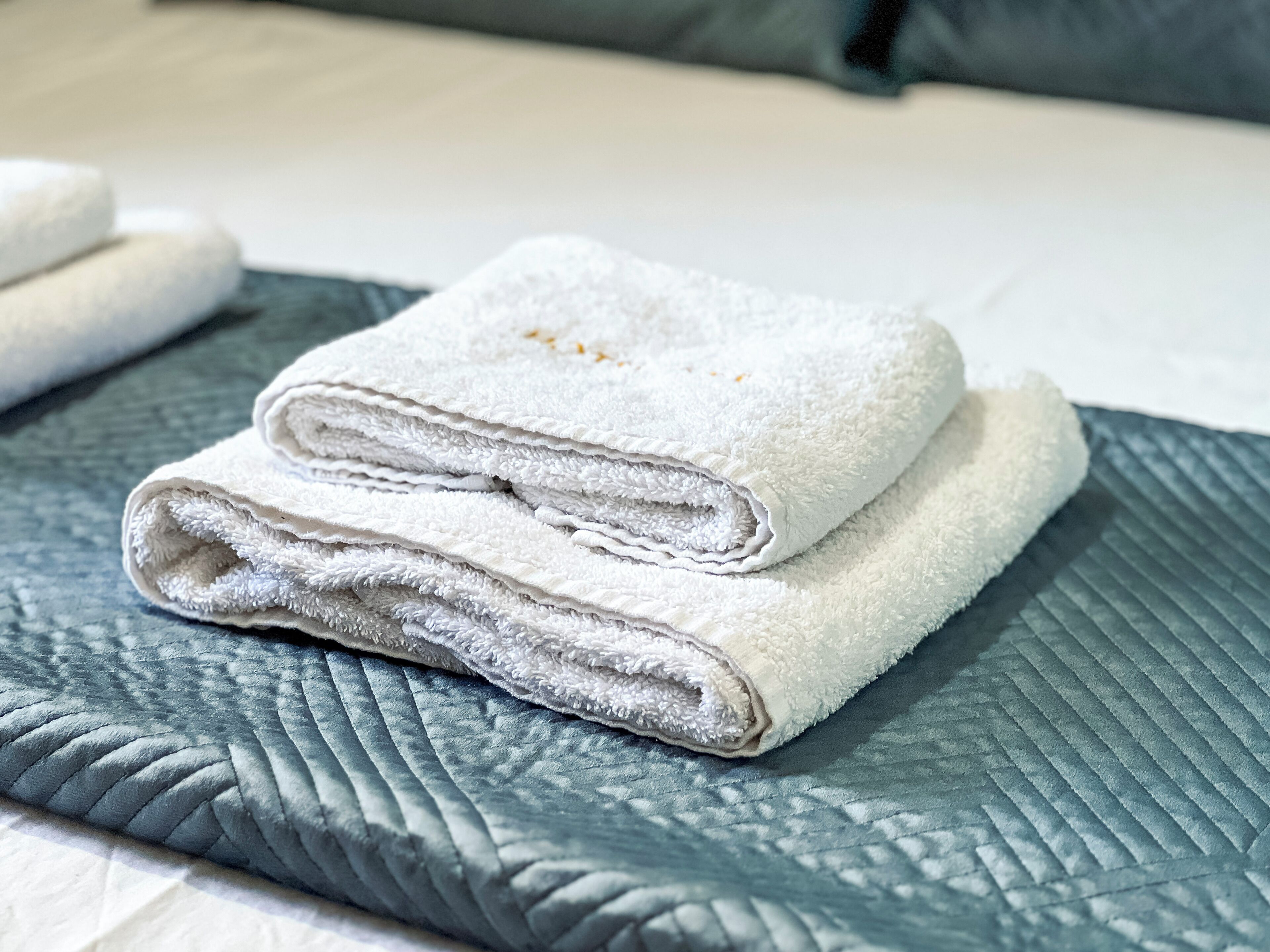 A neatly folded white towel on a textured gray bedspread.