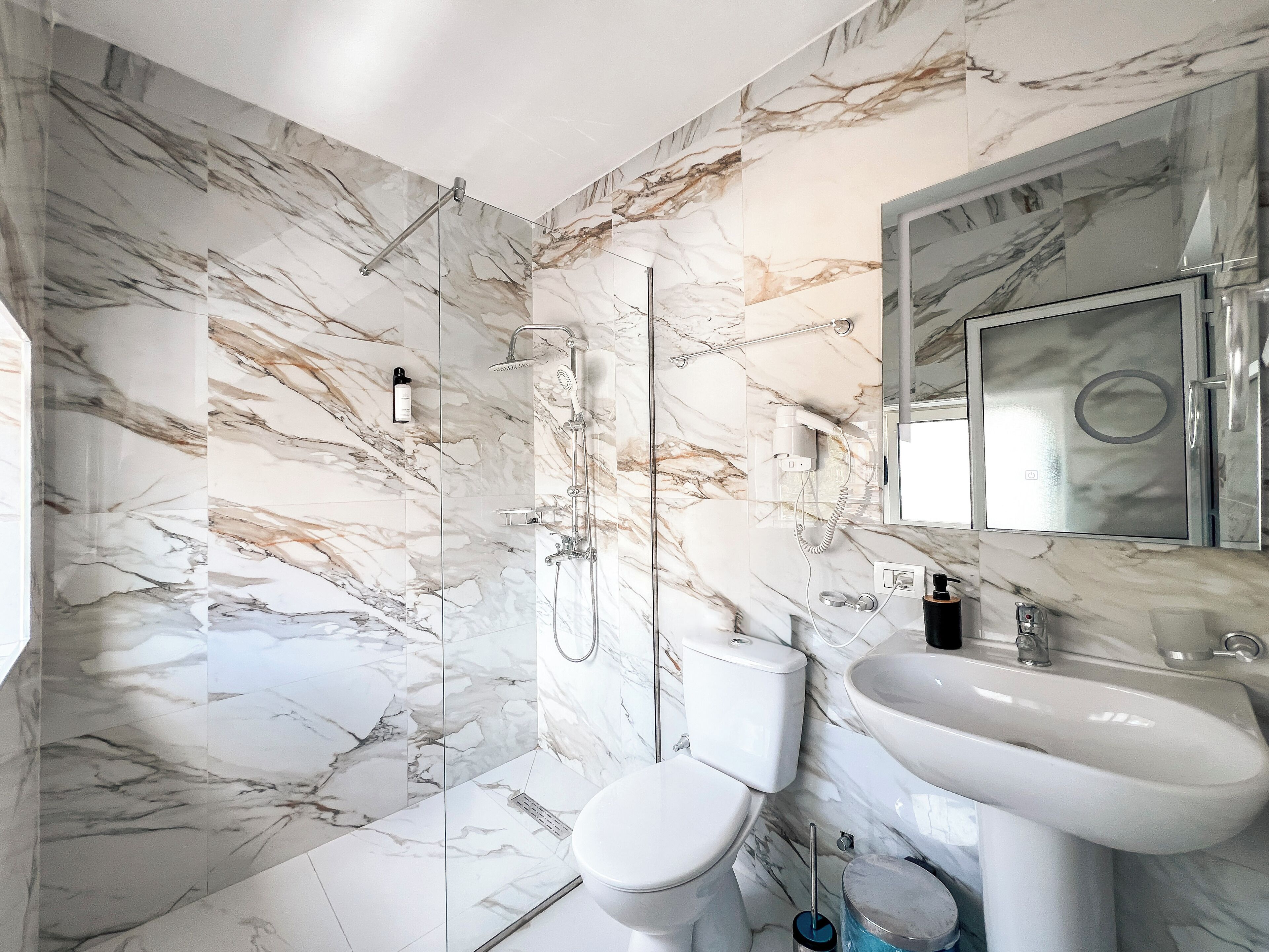 A bathroom with a marble wall, a toilet, a sink, and a shower.