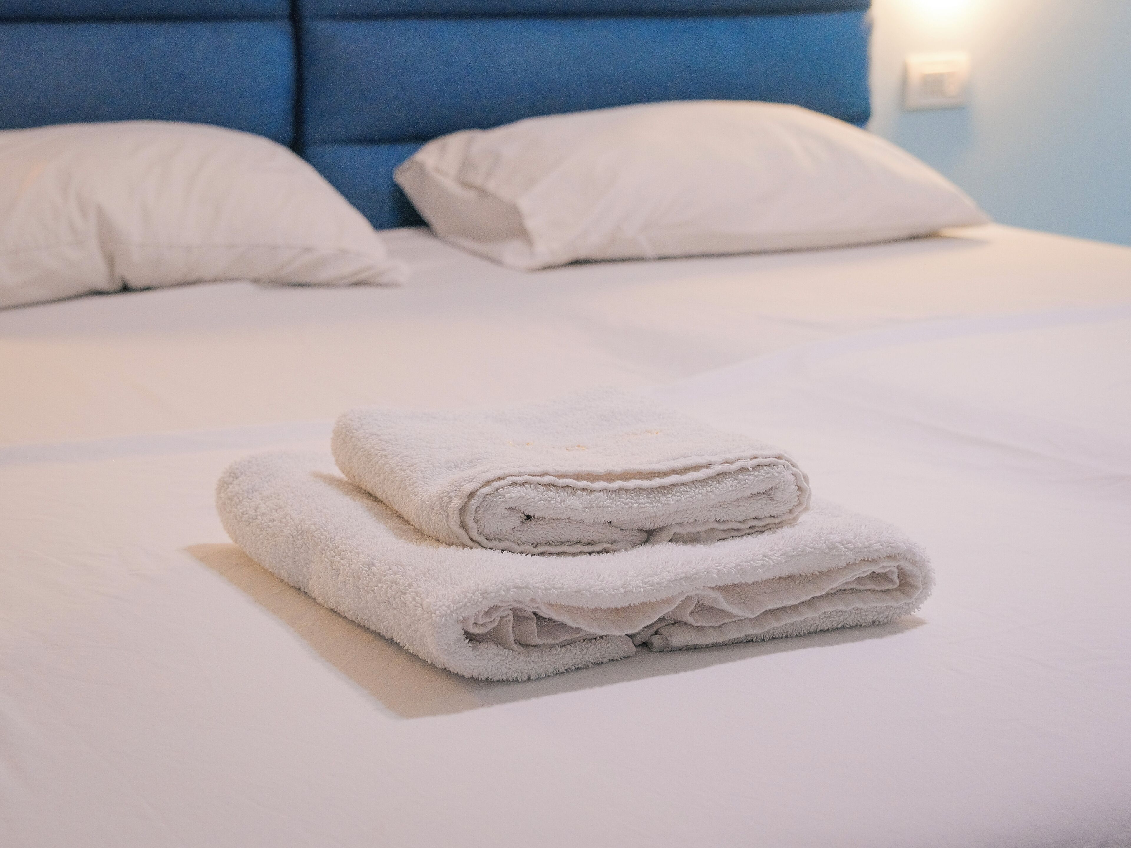 A neatly made bed with white linens and two folded towels on top.