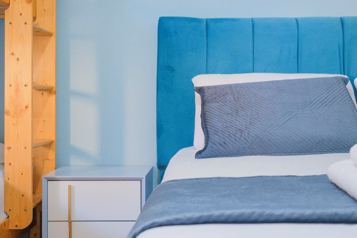 A bed with a blue headboard, a white nightstand, and a wooden wardrobe.