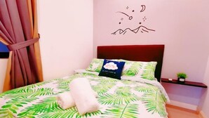 Un lit bien fait, recouvert d’une courtepointe à motifs tropicaux, avec une serviette blanche et un autocollant décoratif sur le mur.